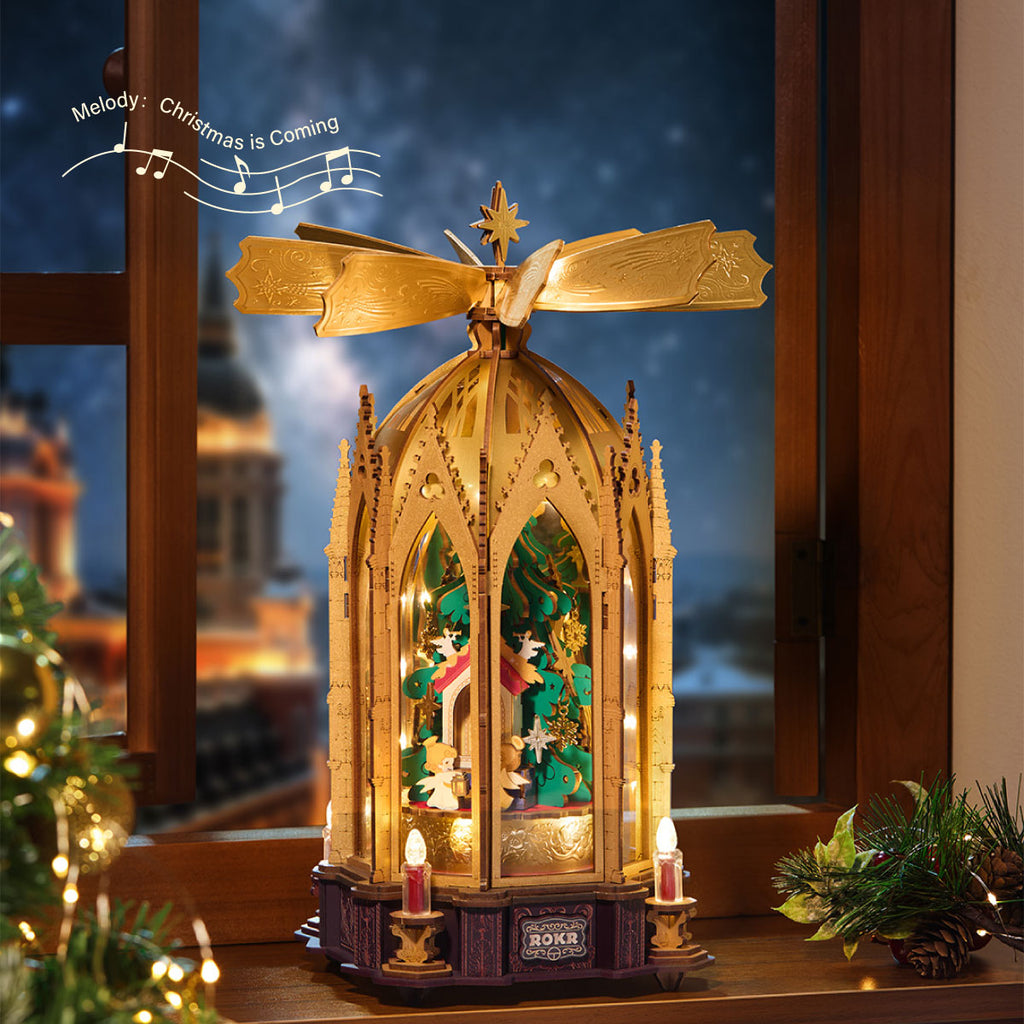 ROKR Angel's Christmas Pyramid displayed beside a window with warm lights, a rotating golden top and a miniature Christmas tree surrounded by angels