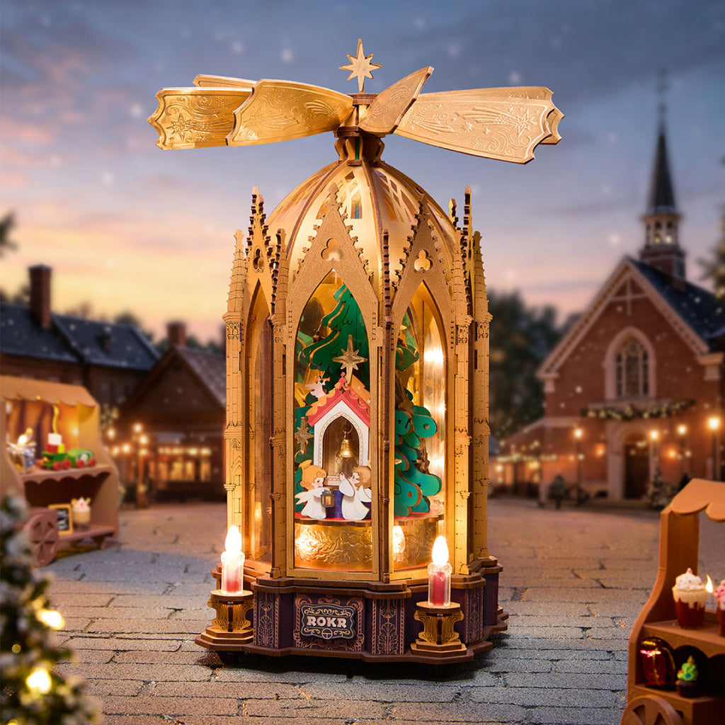 ROKR Angel's Christmas Pyramid illuminated in a miniature winter village setting with snowy rooftops, warm lights and a golden rotating top