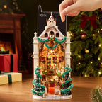 Rolife Caroling Cathedral book nook with its transparent protective dust cover being fitted over the illuminated miniature cathedral