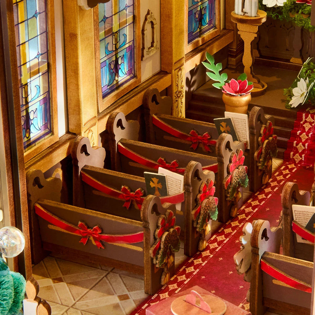 Rolife Caroling Cathedral close-up of miniature wooden pews with red ribbon bows, hymn books, stained glass windows and a red carpet aisle
