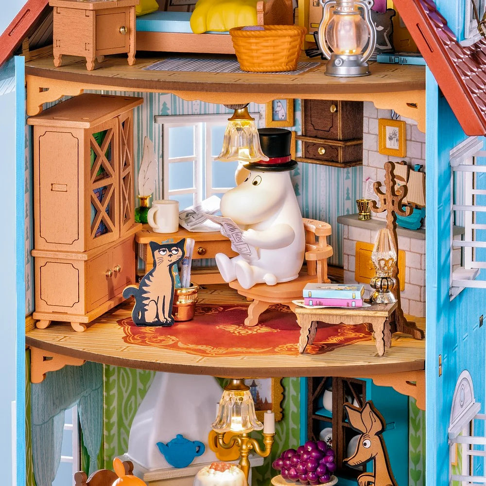 Rolife Moominhouse miniature study featuring Moominpappa reading at a desk, a cat figure, wooden cabinets, books and warm hanging lights
