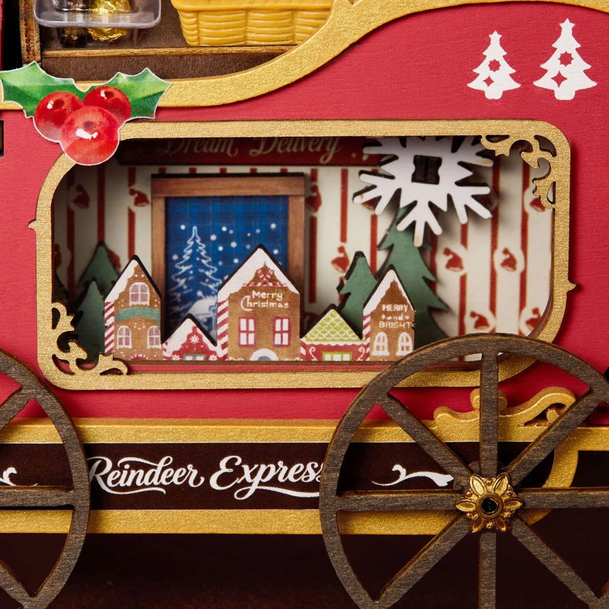 Rolife Reindeer Express close-up showing the red and gold sleigh side panel, decorative holly, wooden wheels and miniature snow-covered Christmas village inside the window