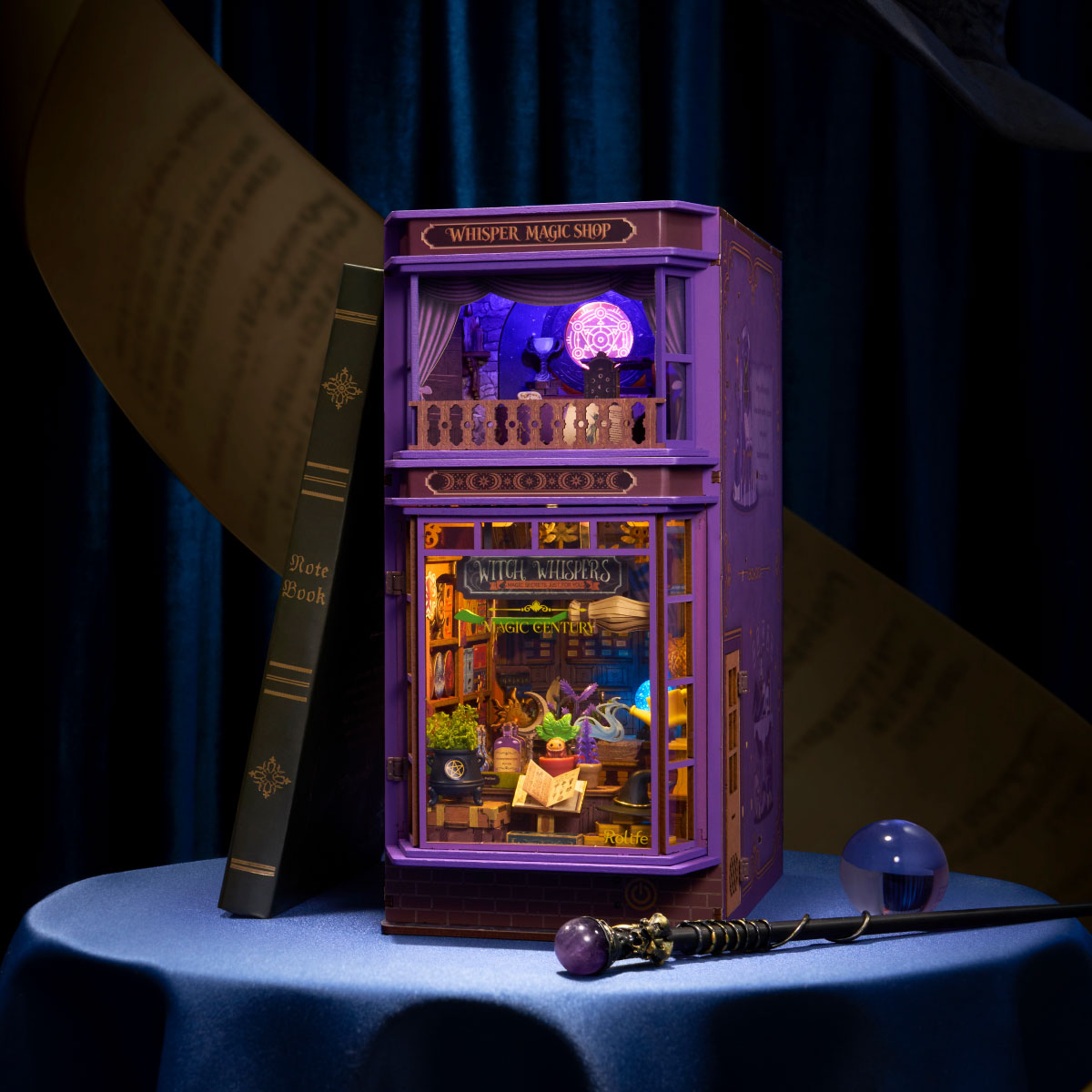 Rolife Whisper Magic Shop DIY book nook illuminated with purple and warm ambient lighting beside fantasy books